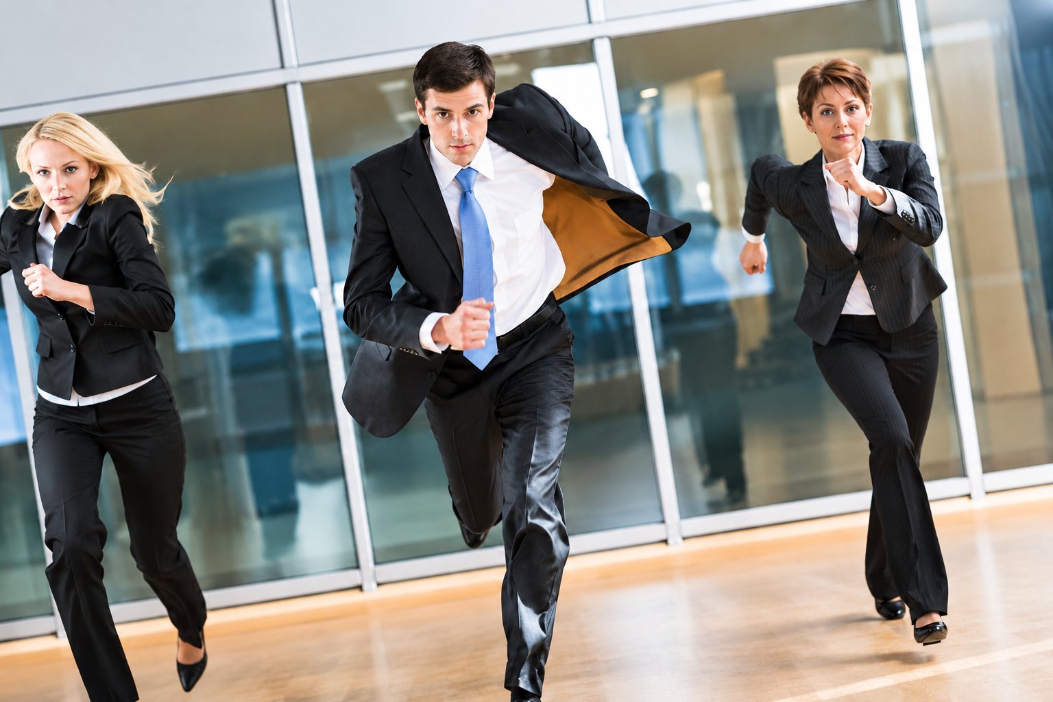 Trois collègues en tenue professionnelle courant dans un couloir de bureau vitré